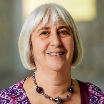Headshot of Sidransky. She is smiling and has short gray hair, a dark necklace, and a purple patterned shirt.