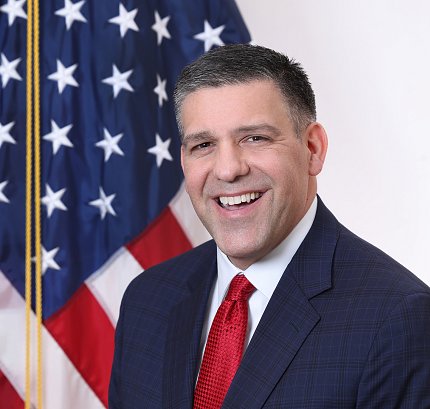 Memoli smiles, in front of U.S. flag