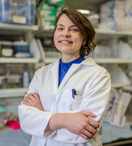 A smiling Gribonika in lab coat, arms folded in an NIH lab