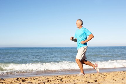 Older man runs on the sand near the ocean.