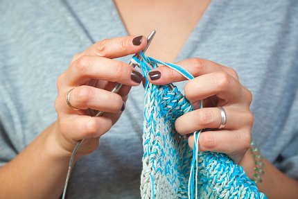 Hands holding crochet needles, knitting blue and white fabric