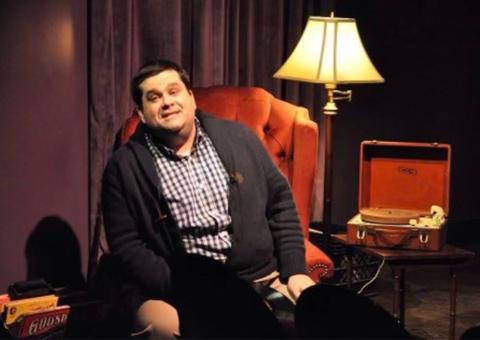 Tittermary seated on stage next to lamp and old turntable and records