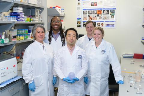 Five members of the BETA team in while lab coats in the lab