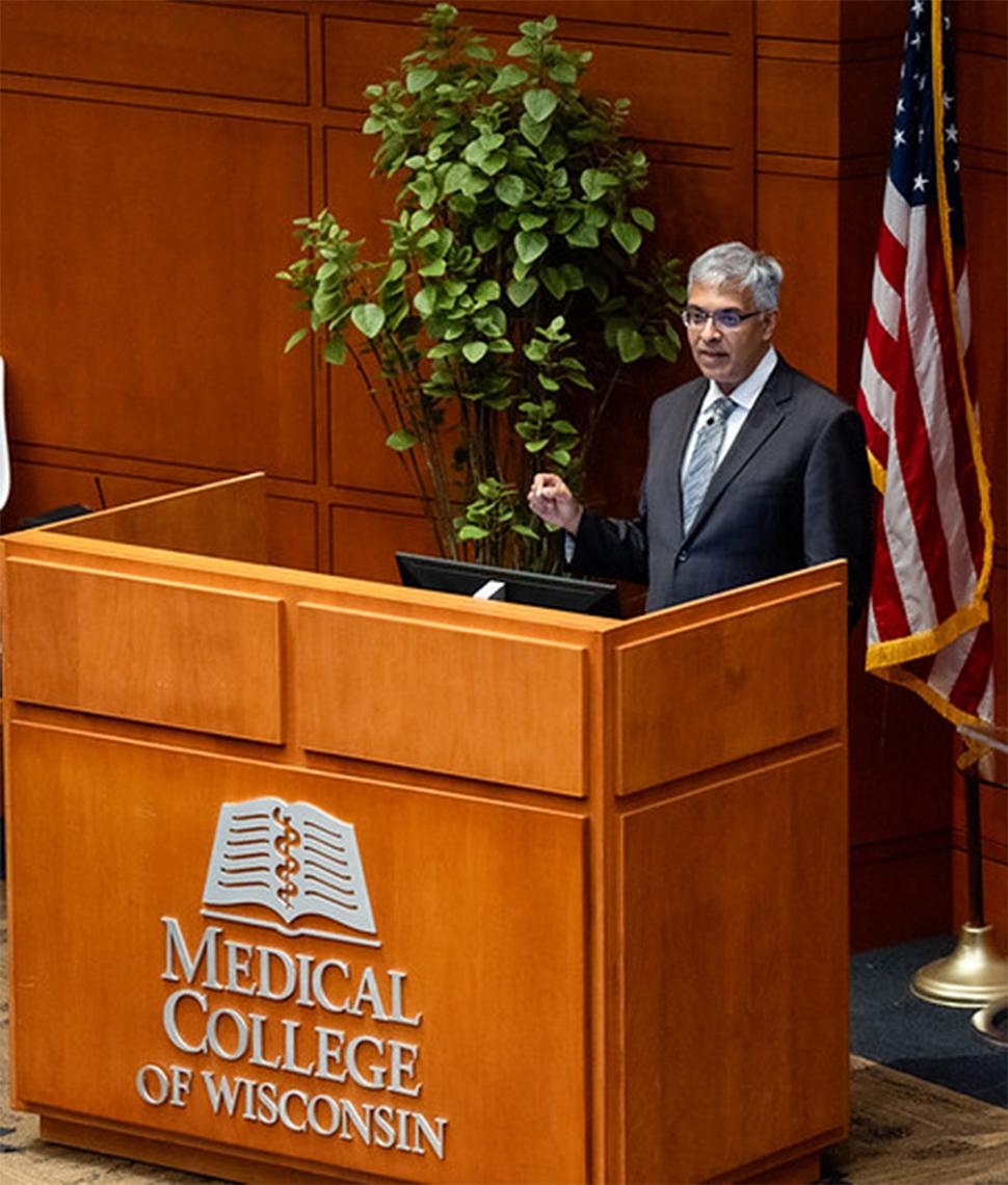 Bhattacharya speaks at a podium