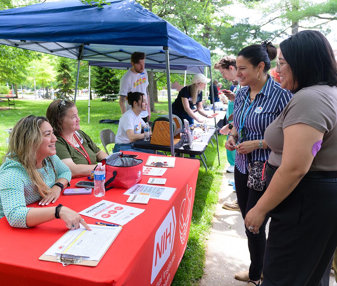 Staff from the NIH Blood Bank sit at a table and speak to attendees.