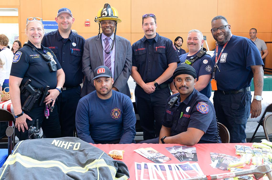 Firefighters pose with Dr. Alfred Johnson, who is wearing a fireman's hat 