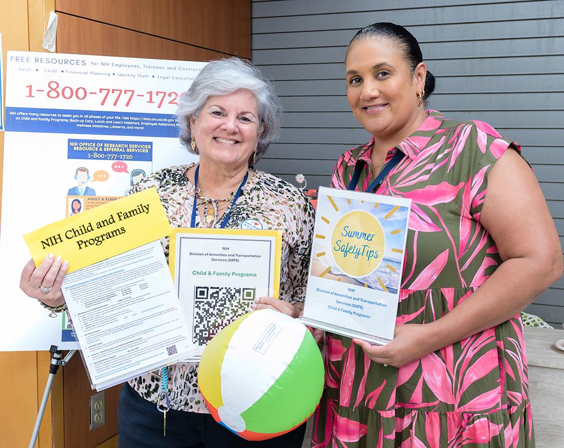 One woman holds child and family programs poster; another holds poster with summer safety tips, and a beach ball