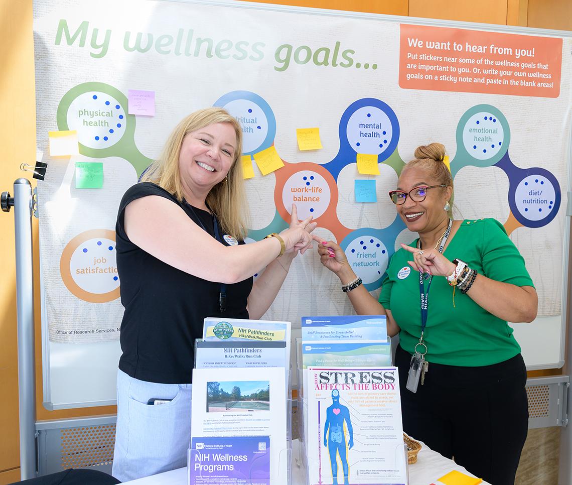 Two smiling women point to "work-life-balance" circle on Wellness Goals poster