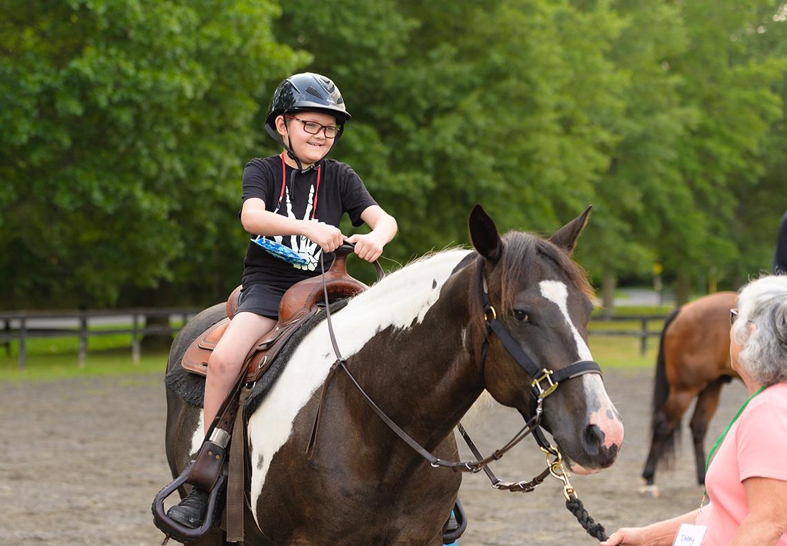 Smiling child in helmet rides a horse.