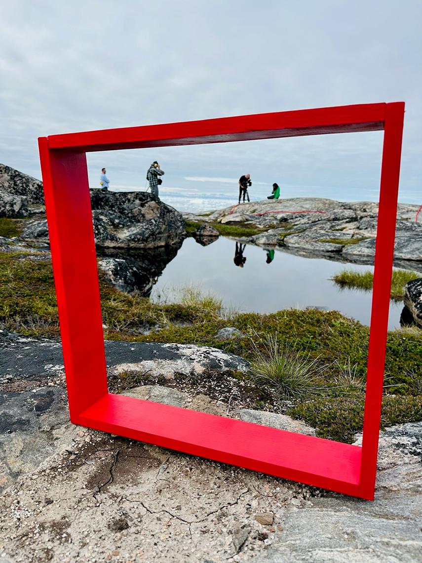 A red frame sits on a rock in Greenland. Scientist conduct field work in the background.