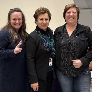 Three women pose together, smiling